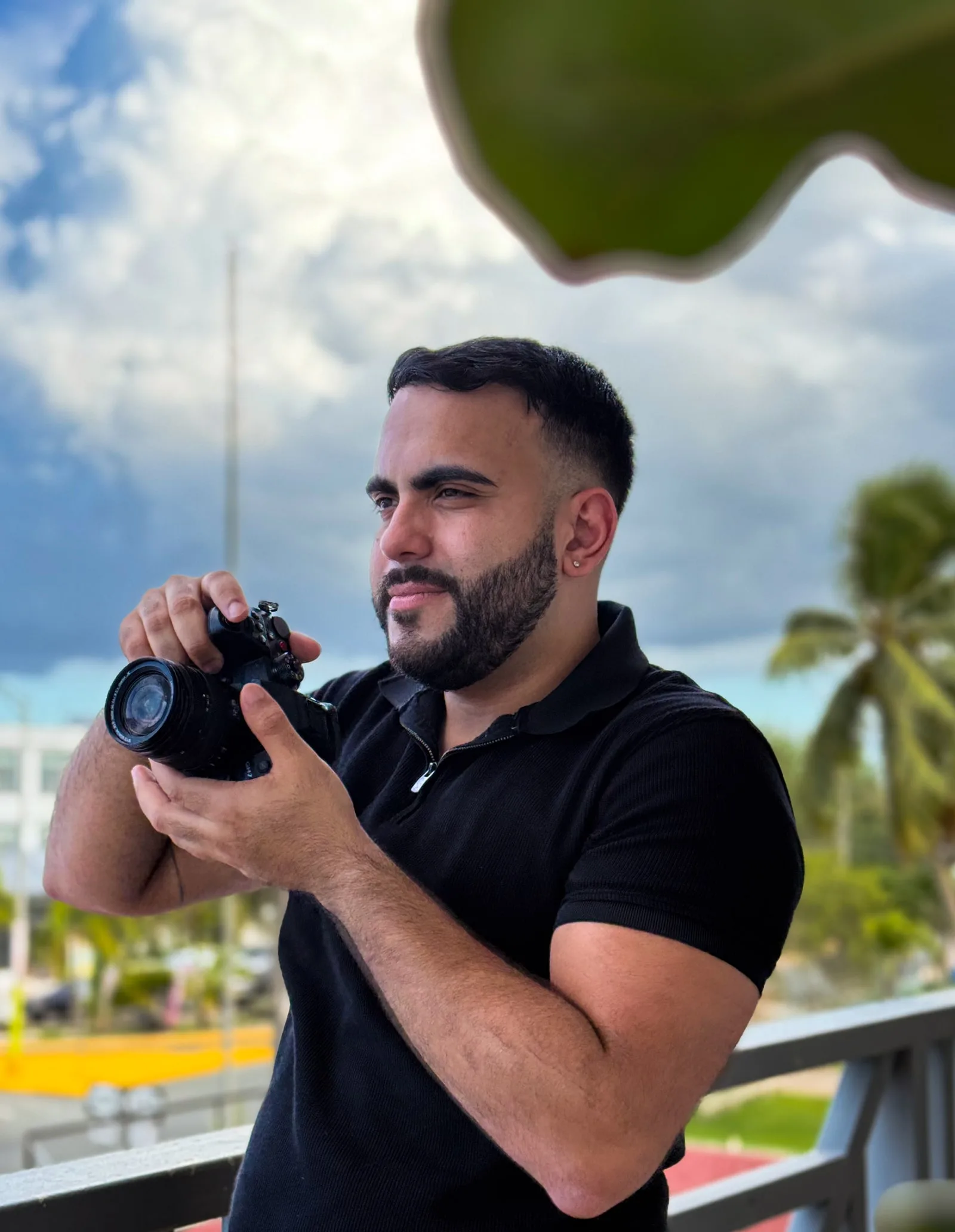 Pedro Villegas, camera in hand on a balcony in front of palm trees